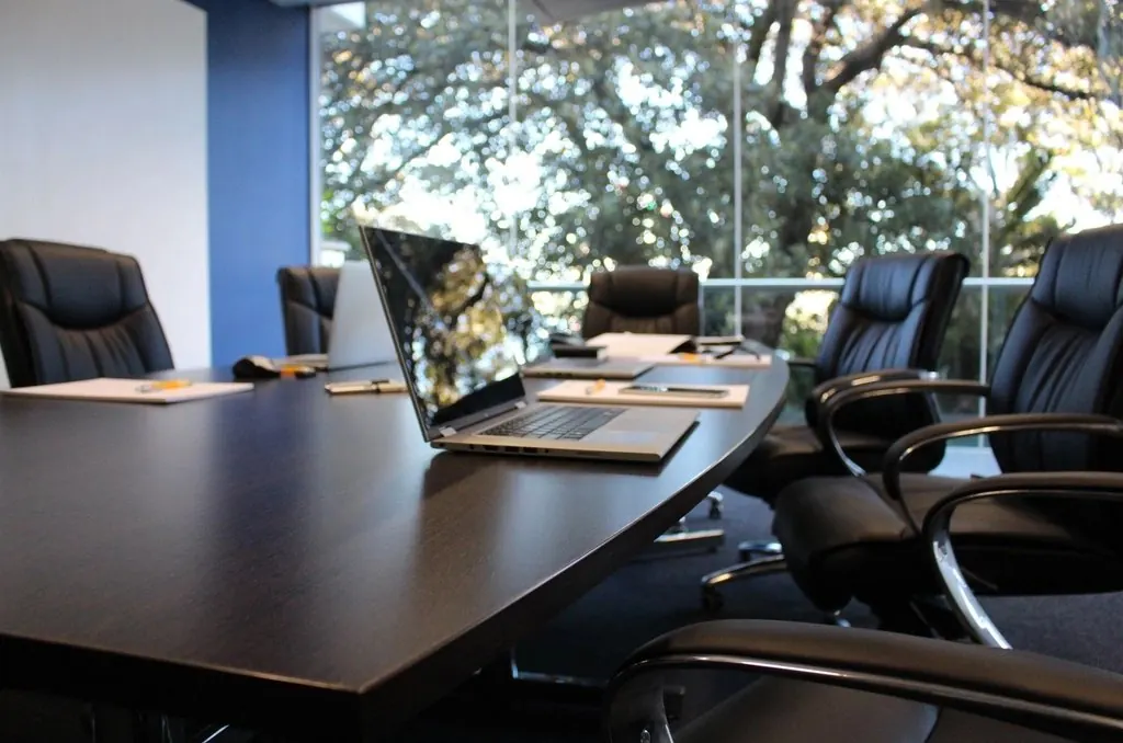 A dark boardroom table under window light — company decisions and the documents that record them