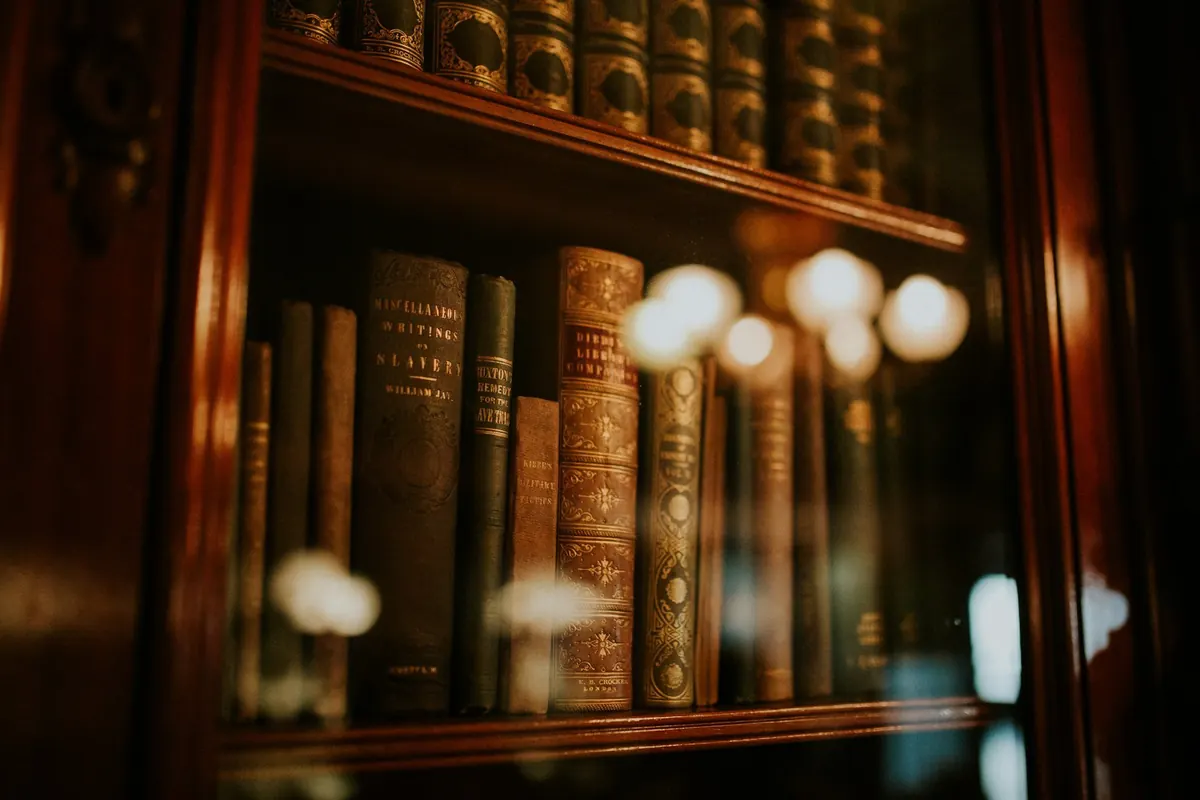 Leather-bound volumes in a glass-fronted bookcase, lamplight reflected in the glass